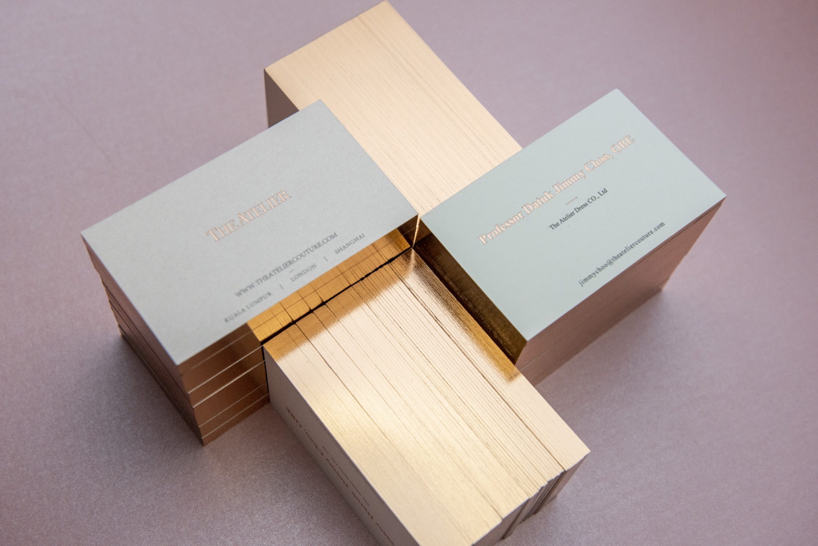 Overlapping pale card stacks reveal reflective copper-coloured edges against a pink background.