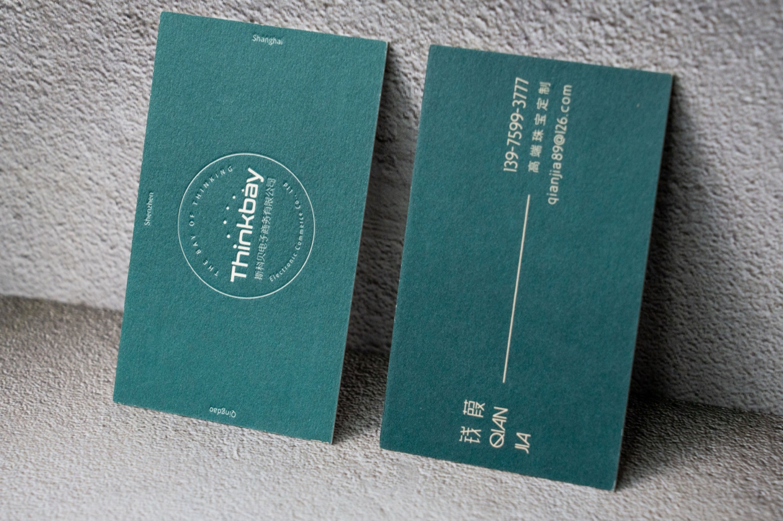 A teal card pair combining a small outlined round mark with gold-coloured contact text.