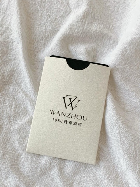 An ivory paper sleeve with a semicircular thumb notch and dark monogram on white fabric.