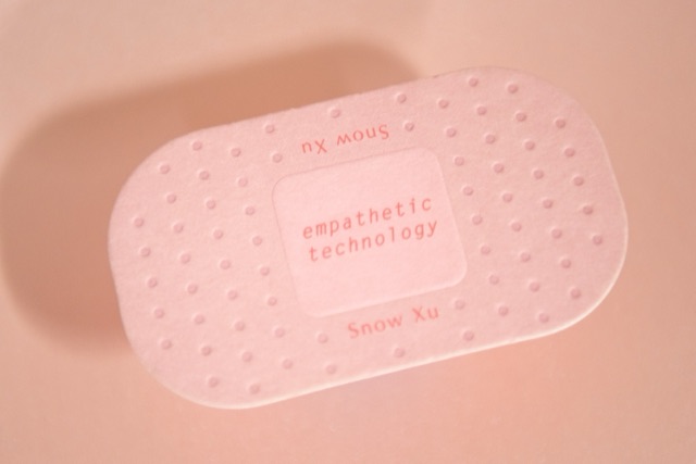 A pale pink oval card with a dotted border and small central lettering.