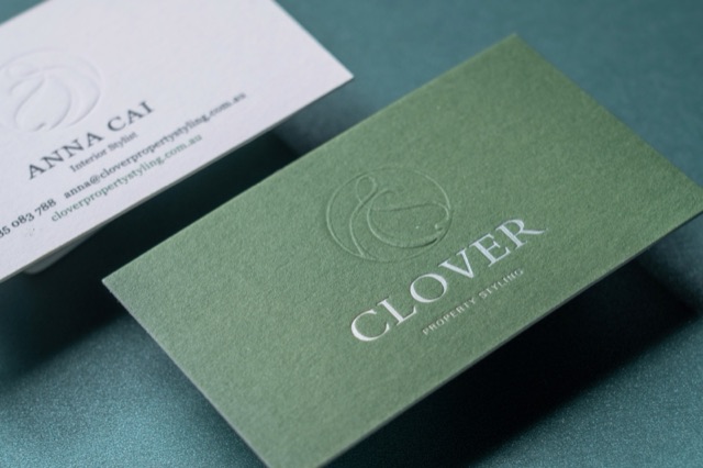 A sage green card with a large subtle monogram beside its white companion card.
